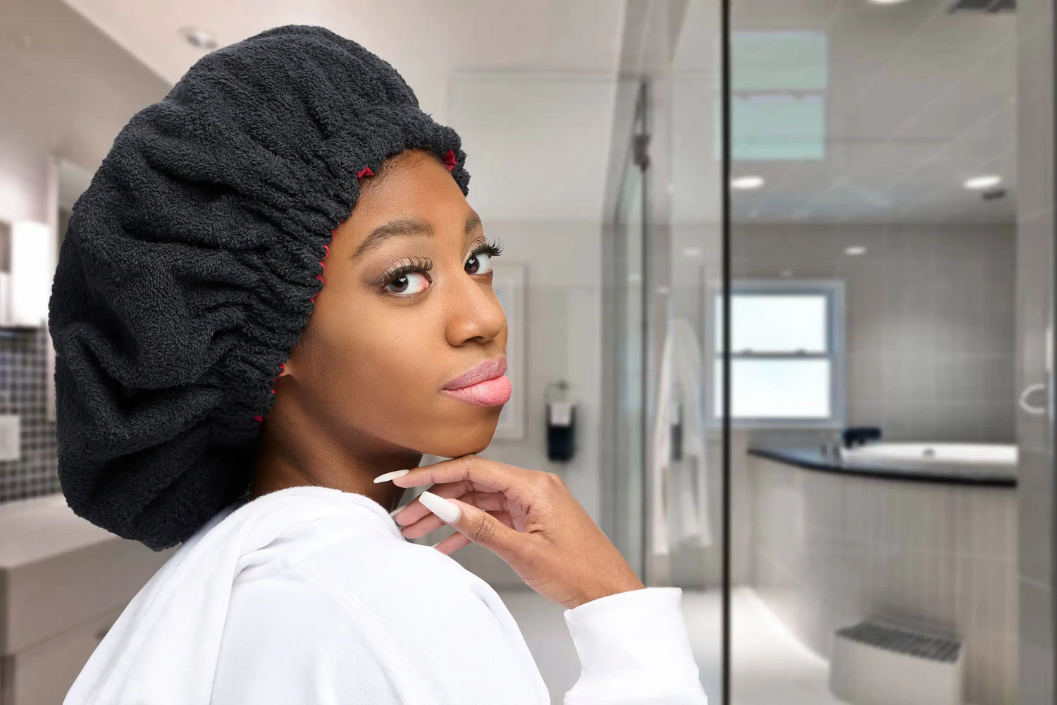 Young African American woman gracefully poses with hand under chin, wearing a Steamy Beenie in a luxurious, spa-inspired bathroom.